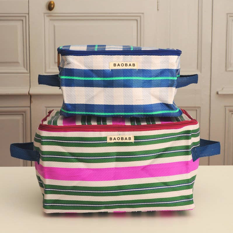 Two striped fabric storage bins stacked on a light surface in front of a paneled cream door. The top bin is blue, teal, and white striped, while the bottom bin is green, pink, and white striped.