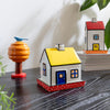 Decorative house models on a dark surface with greenery in the background