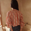 Person wearing a patterned blouse and jeans, holding a brown handbag in a bathroom.