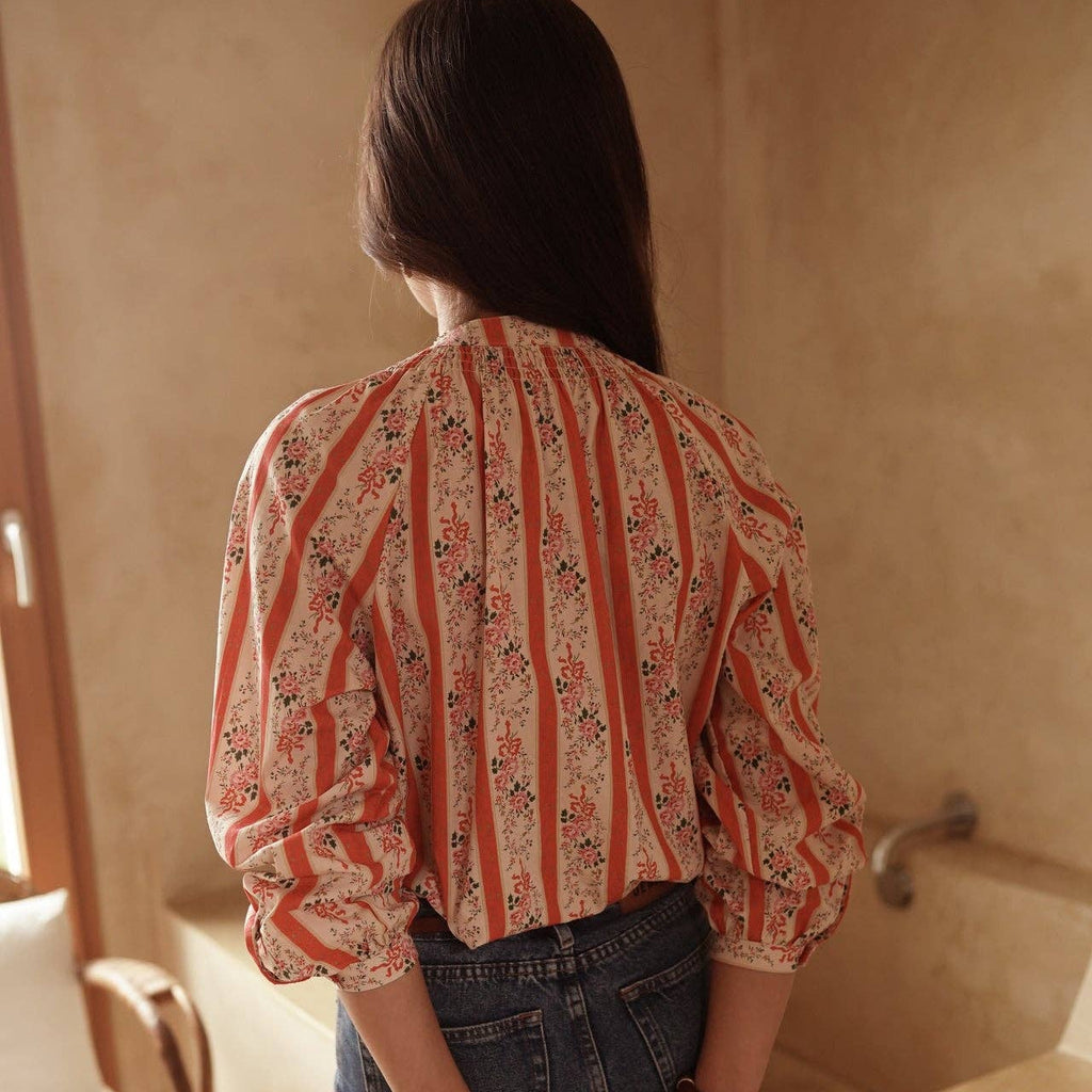 Person wearing a patterned blouse and jeans, holding a brown handbag in a bathroom.