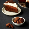 Chocolate cake slice with whipped cream on a white plate, surrounded by chocolate truffles on a dark surface.