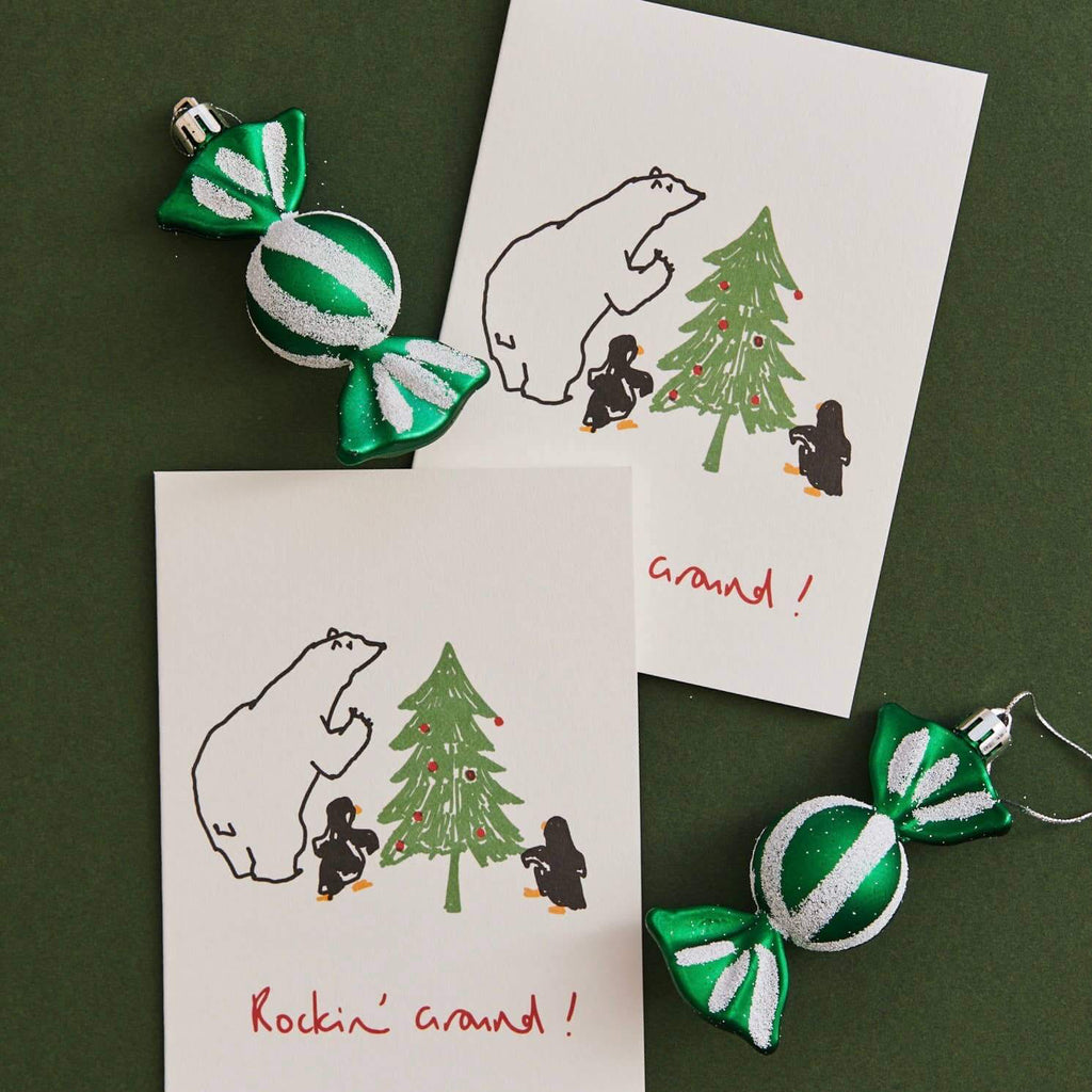 Two Christmas cards with polar bear and tree illustrations, accompanied by green and white candy ornaments on a dark green background.