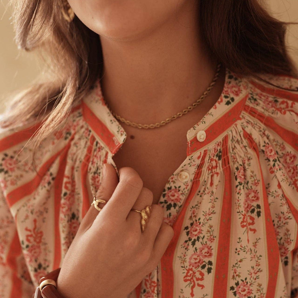 Close-up of a person wearing a floral blouse with jewelry and hair accessories.