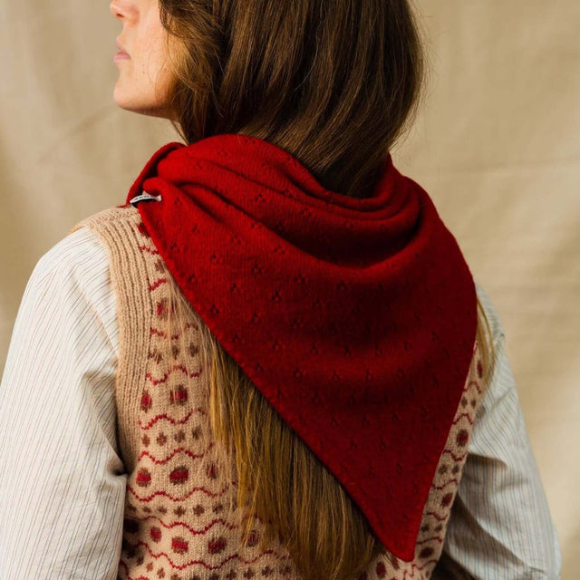 Person wearing a red knitted scarf over a patterned vest against a beige background