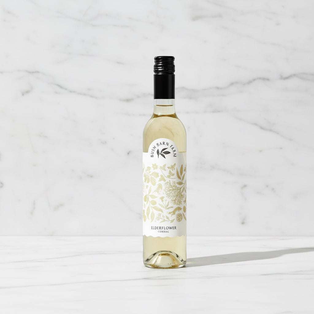 Bottle of Elderflower wine with a glass on a wooden table outdoors.