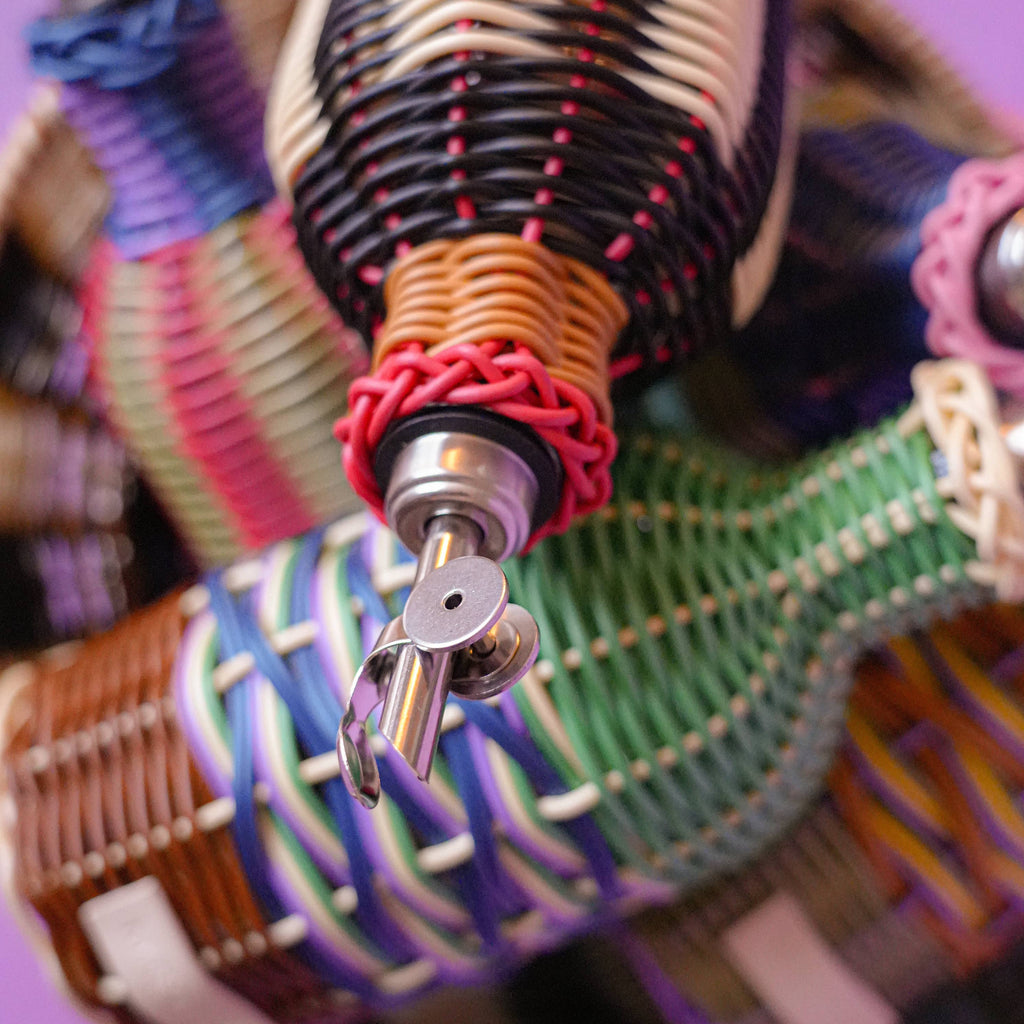 Colorful woven bottle holder with a key on a pink background