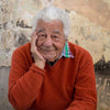 Man in an orange sweater sitting at a table with a textured wall background