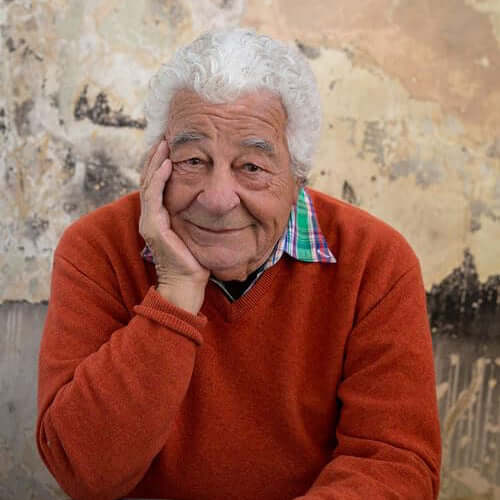 Man in an orange sweater sitting at a table with a textured wall background