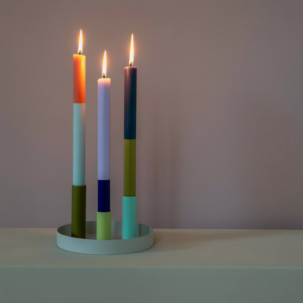 Colorful candle holder with three lit candles on a table next to books and a plate of cookies.