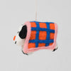 A handcrafted felt dog ornament wrapped in a plaid blanket with orange, blue, and pink colors, hanging against a light gray background.