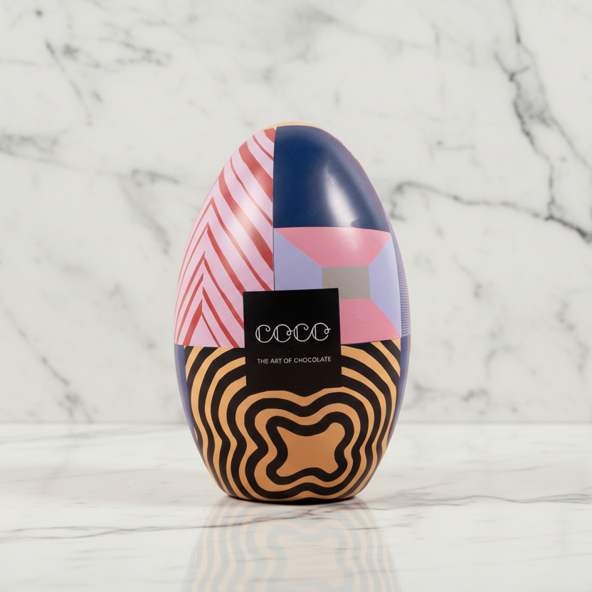Colorful chocolate egg with geometric patterns on a pink background, featuring the brand 'Coco'.