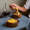 Person lifting a spoonful of cheesy soup from a bowl on a table with wine glasses.