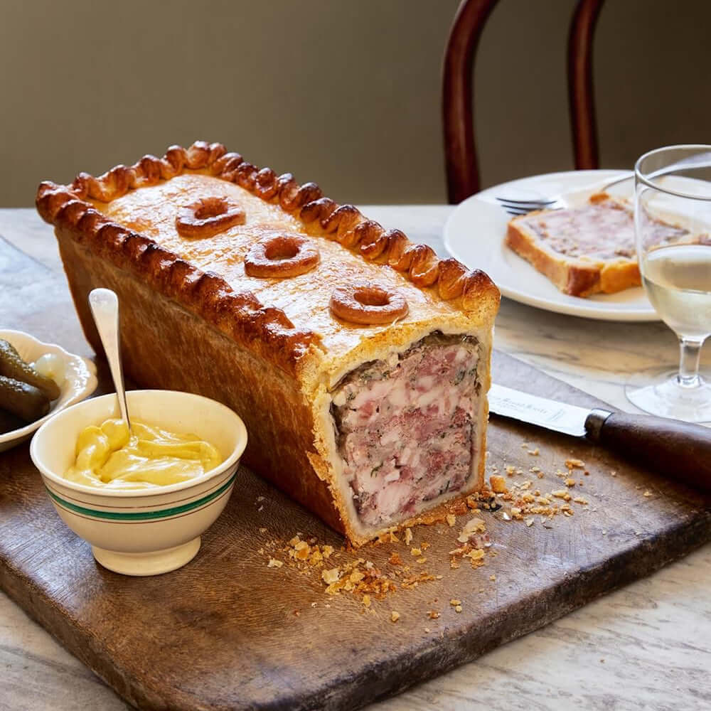 Meatloaf with a slice cut out on a wooden board, served with butter and a glass of wine.