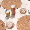 Cork placemats and coasters on a white table with glasses and candles.