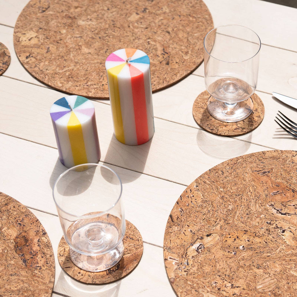 Cork placemats and coasters on a white table with glasses and candles.