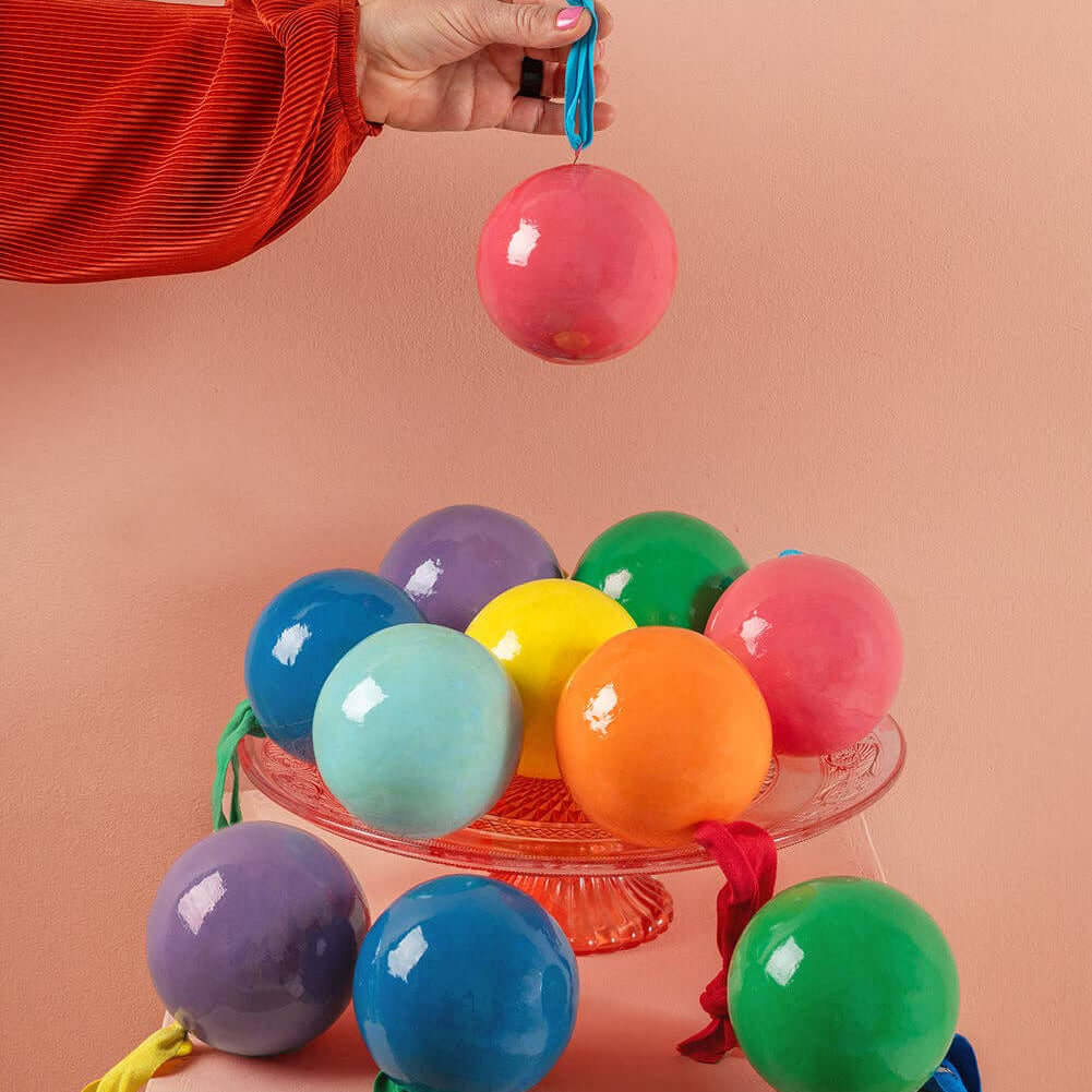 Colorful balloons on a cake stand with a hand holding a pink balloon against a peach background