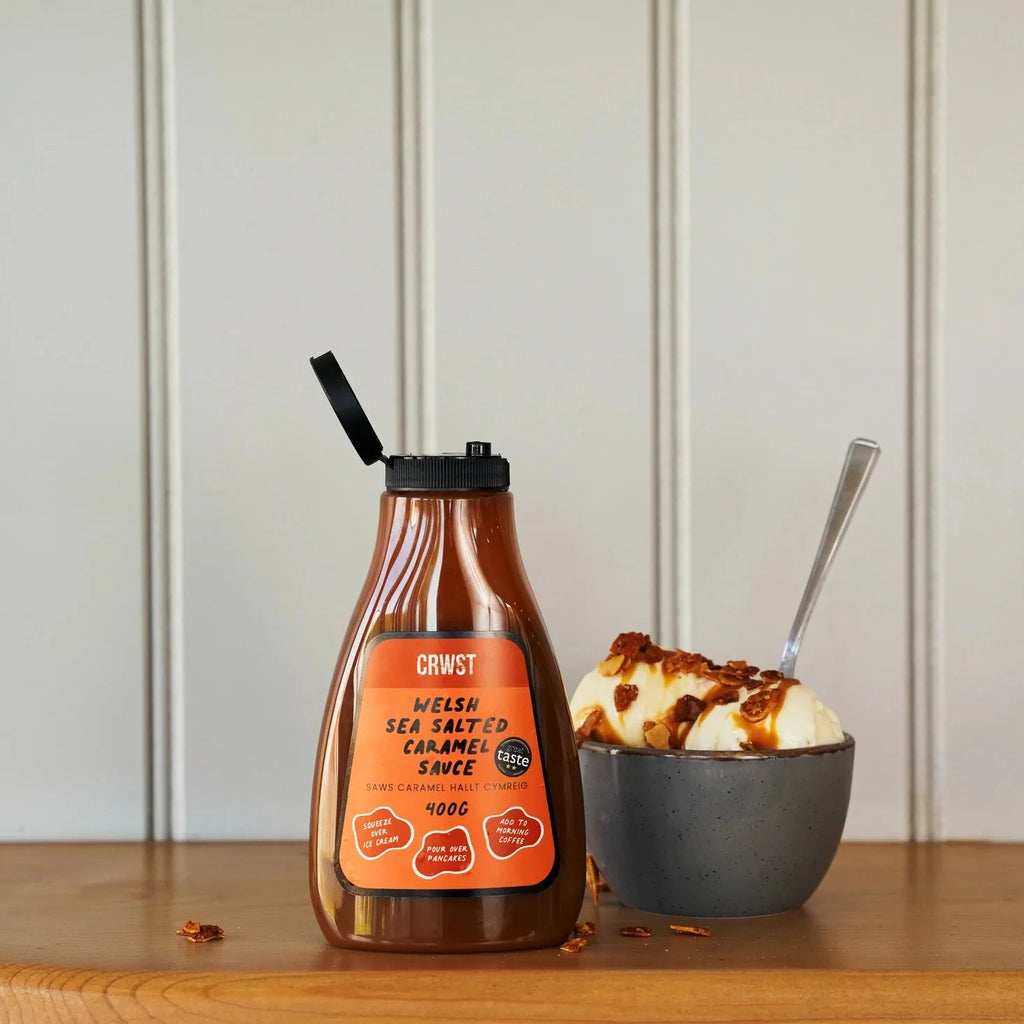 Bottle of sauce with a label next to a bowl of ice cream on a wooden surface.