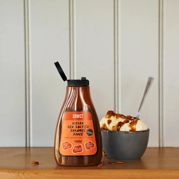 Bottle of sauce with a label next to a bowl of ice cream on a wooden surface.