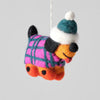 A felted wool dachshund hanging ornament wearing a pink and teal plaid sweater, a teal and white beanie hat, and orange paws, suspended by a white string against a solid gray background.
