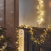 Decorative string lights on a mantelpiece with a candle and Christmas tree.