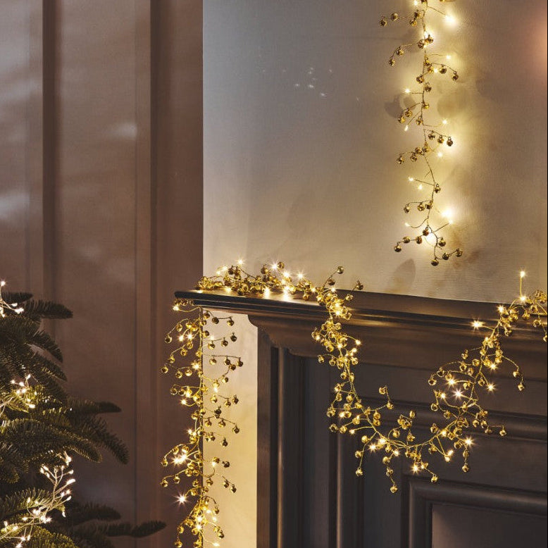 Decorative string lights on a mantelpiece with a candle and Christmas tree.