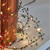 Decorative string lights with red and green berries on a white surface