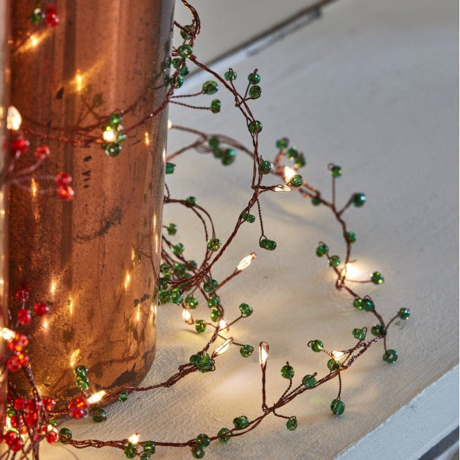 Decorative string lights with red and green berries on a white surface