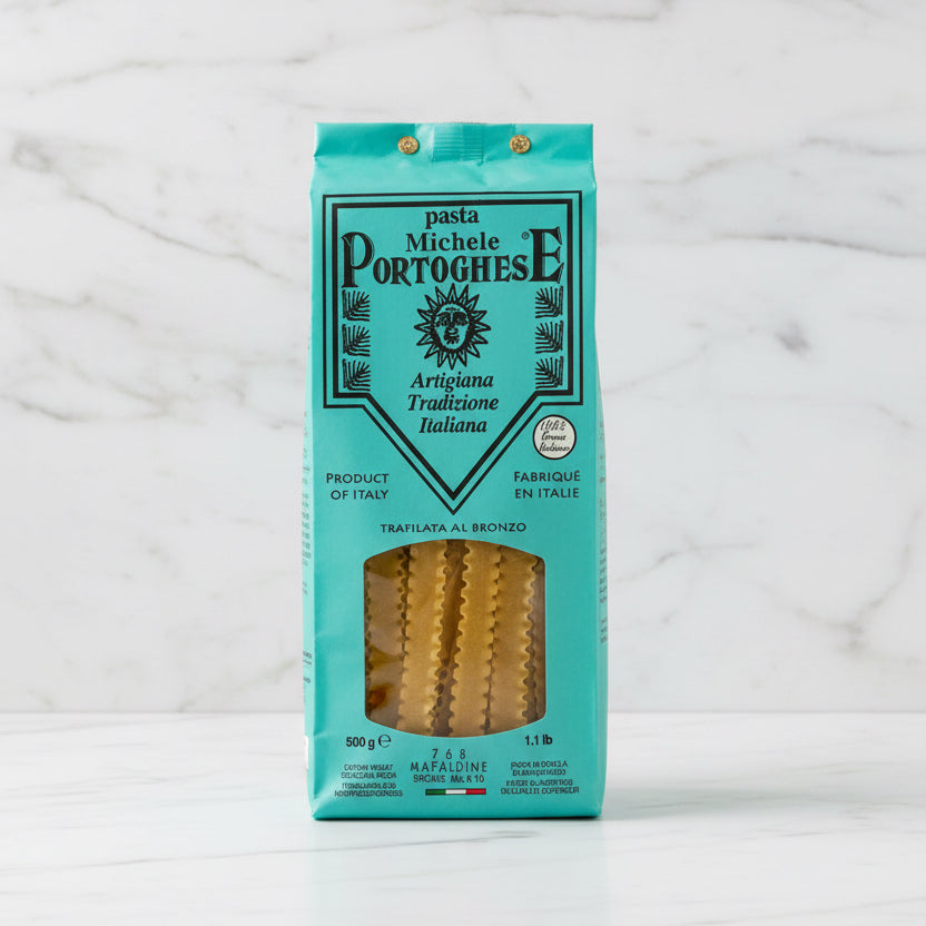 A 500g package of Michele Portoghese Artigiana Tradizione Italiana pasta, featuring a turquoise and black design with a clear window showing the ridged yellow pasta inside.