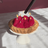 Tart with raspberries acting as candles on a white stand against a white background