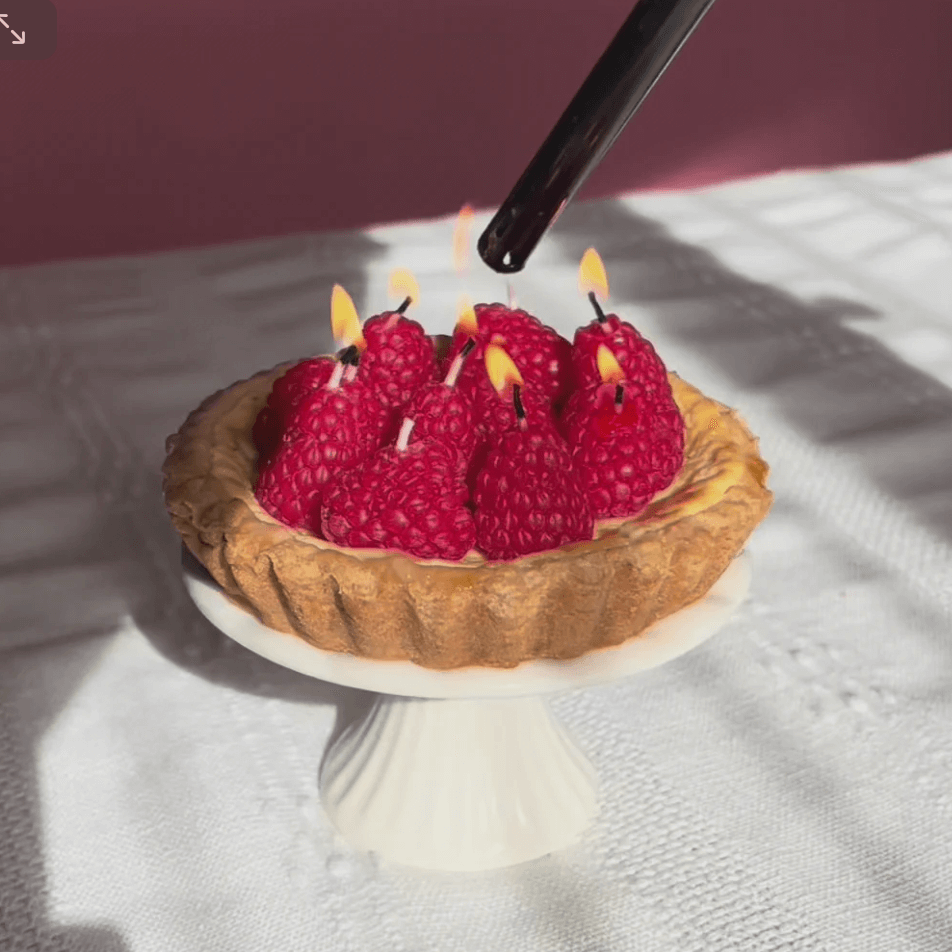 Tart with raspberries acting as candles on a white stand against a white background