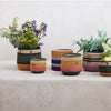 A set of six hand-painted ceramic planters with colorful Southwestern-style stripes, arranged on a light stone surface against a neutral off-white wall.