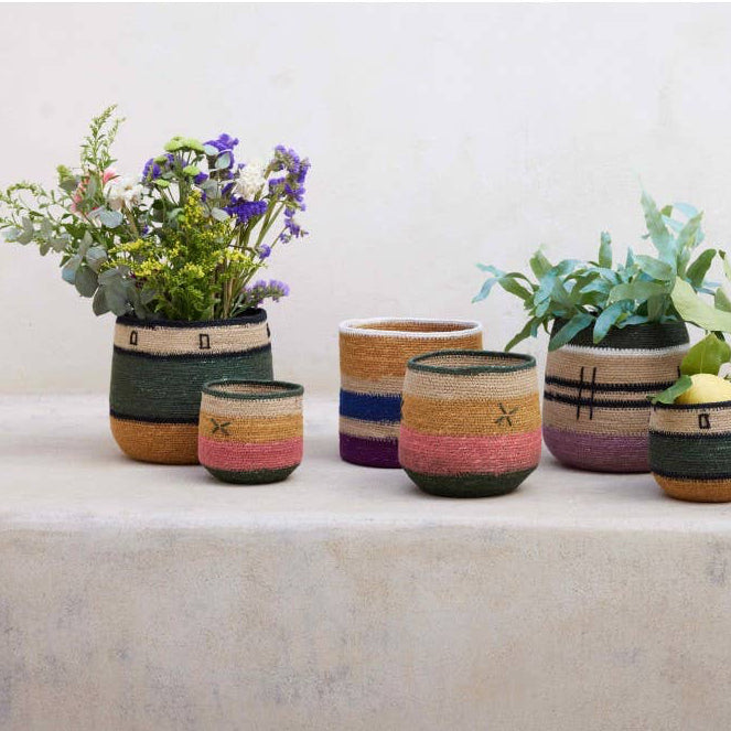 A set of six hand-painted ceramic planters with colorful Southwestern-style stripes, arranged on a light stone surface against a neutral off-white wall.