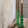 Two green candle holders with lit candles on a wooden surface.