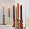 Colorful candles in various candlesticks on a white surface