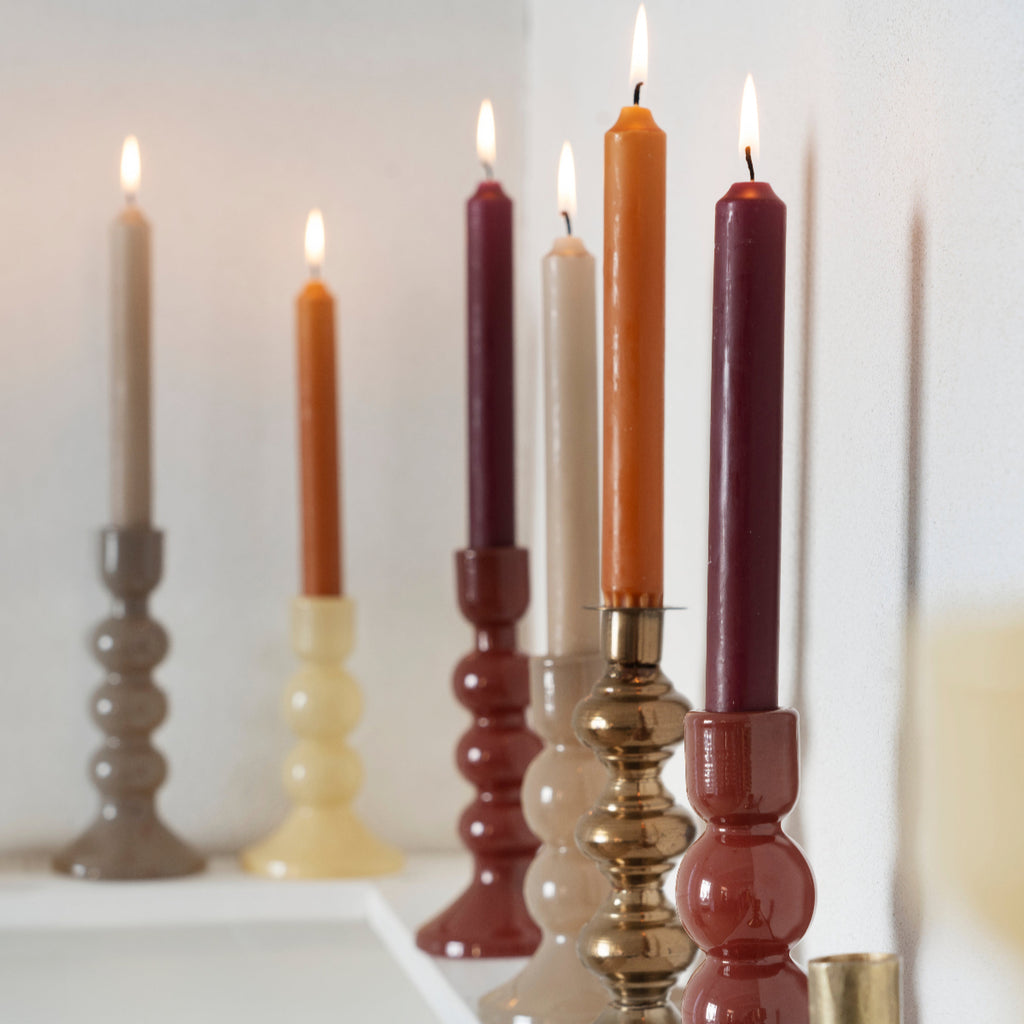 Colorful candles in various candlesticks on a white surface