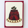 Card with a festive cake design featuring a red bow and holly on a white background