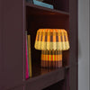 Small lamp with a striped design on a shelf next to books and a cereal box.