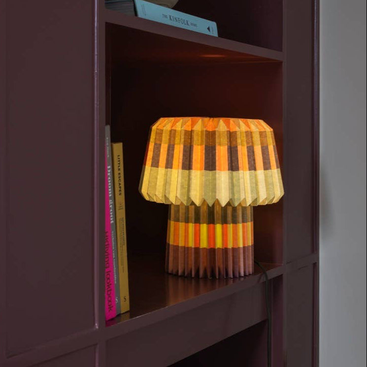 Small lamp with a striped design on a shelf next to books and a cereal box.