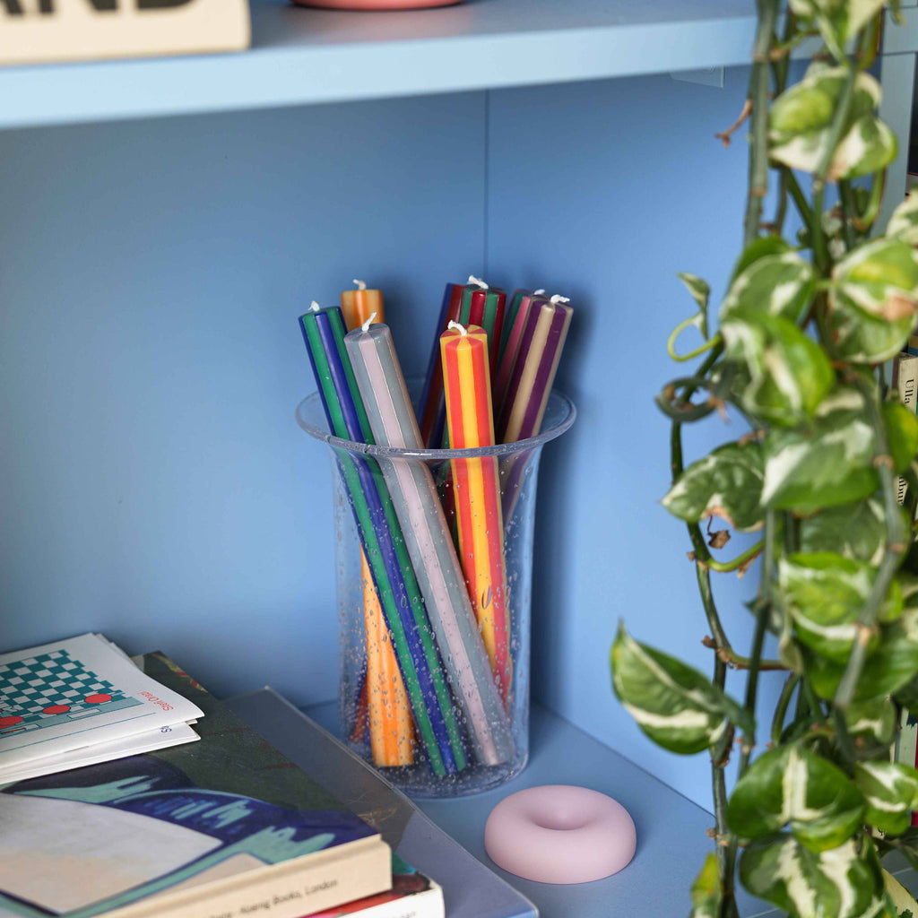 Colorful pencils in a clear cup on a blue shelf with books and decorative items.
