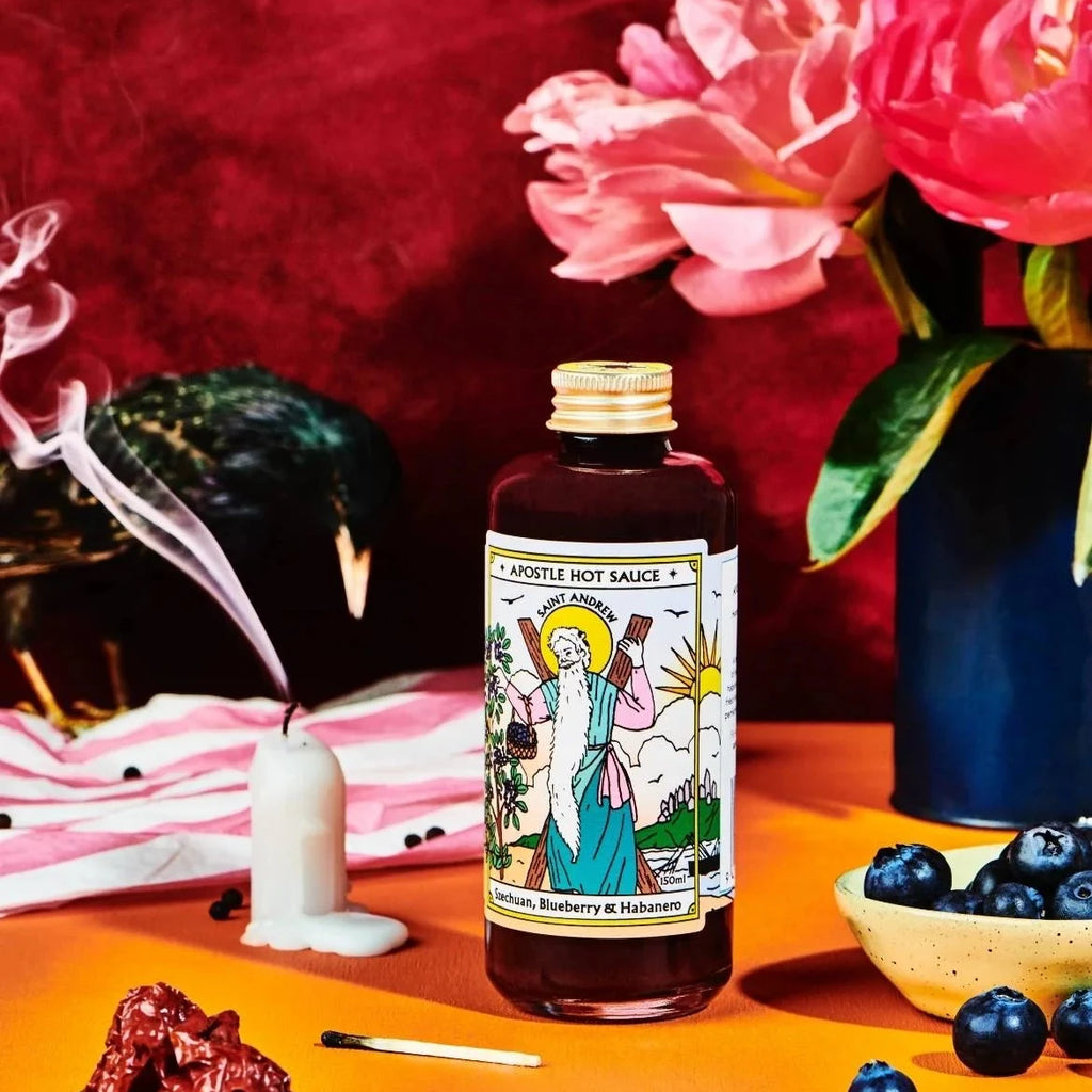 Hot sauce bottle with decorative label on an orange surface with flowers and candles