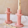 Pink candle holder with a white candle labeled 'all you need is love' on a beige background