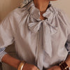 Woman wearing a striped blouse with bow details against a neutral background