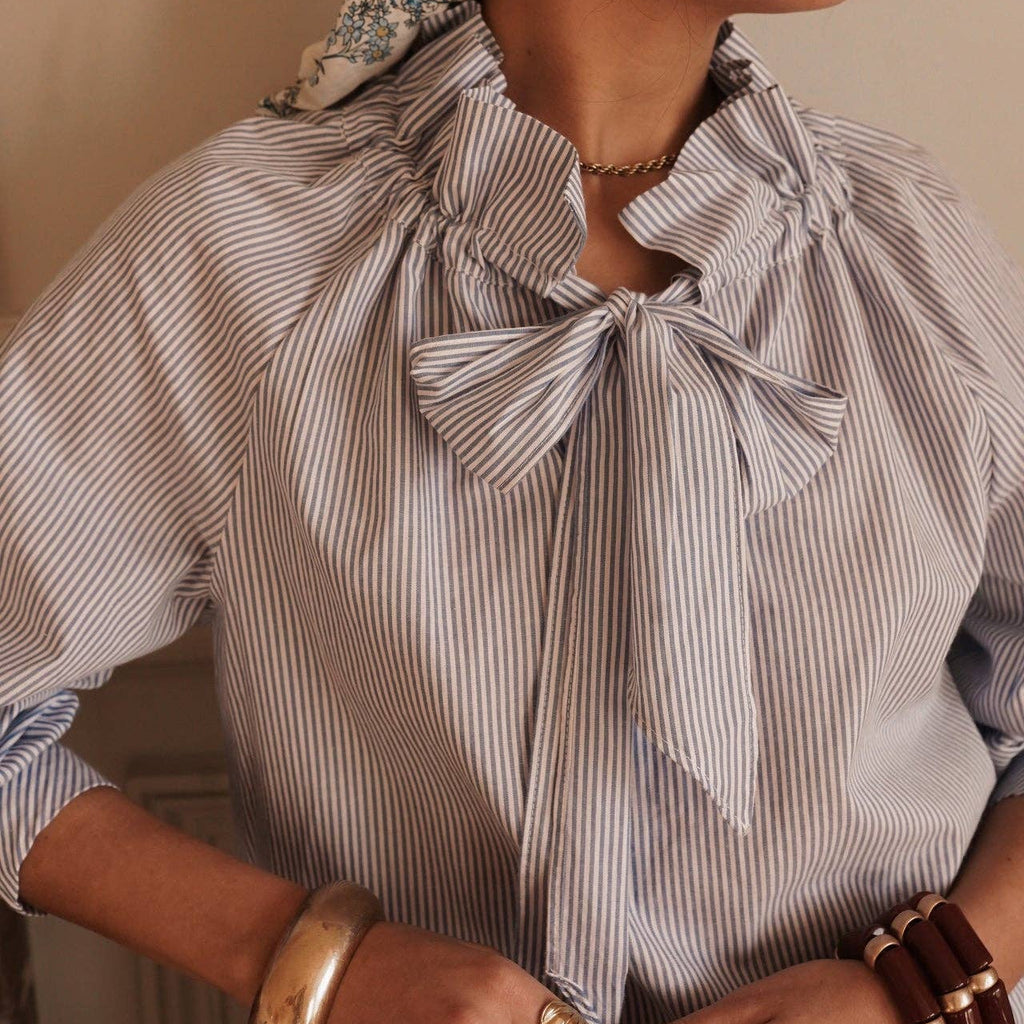 Woman wearing a striped blouse with bow details against a neutral background