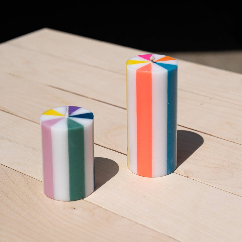Two colorful cylindrical candles on a wooden surface with a black background