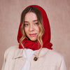 Woman wearing a red hooded garment over her head against a beige background