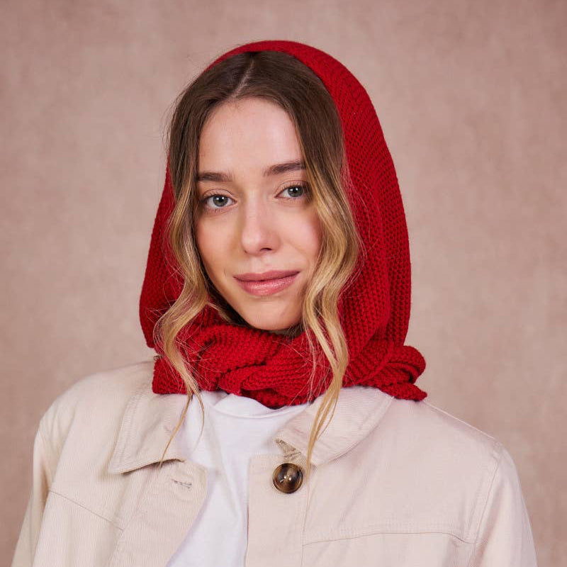 Woman wearing a red hooded garment over her head against a beige background