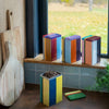 Colorful cookie tins on a windowsill with cookies on a cooling rack below.