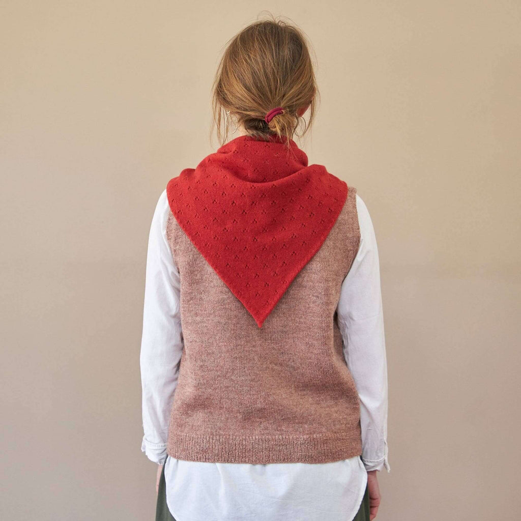 Person wearing a brown vest with a red hood against a beige background