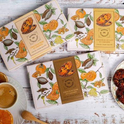 Candle boxes with orange and leaf design on a rustic wooden surface with cookies and coffee.