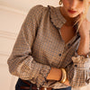 A woman wearing a beige and brown plaid button-down blouse with ruffled trim, tucked into dark blue jeans with a brown belt.